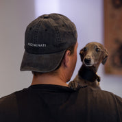 Person wearing a cap with 'IGGYMINATI' and a dog on their shoulder against a neutral background