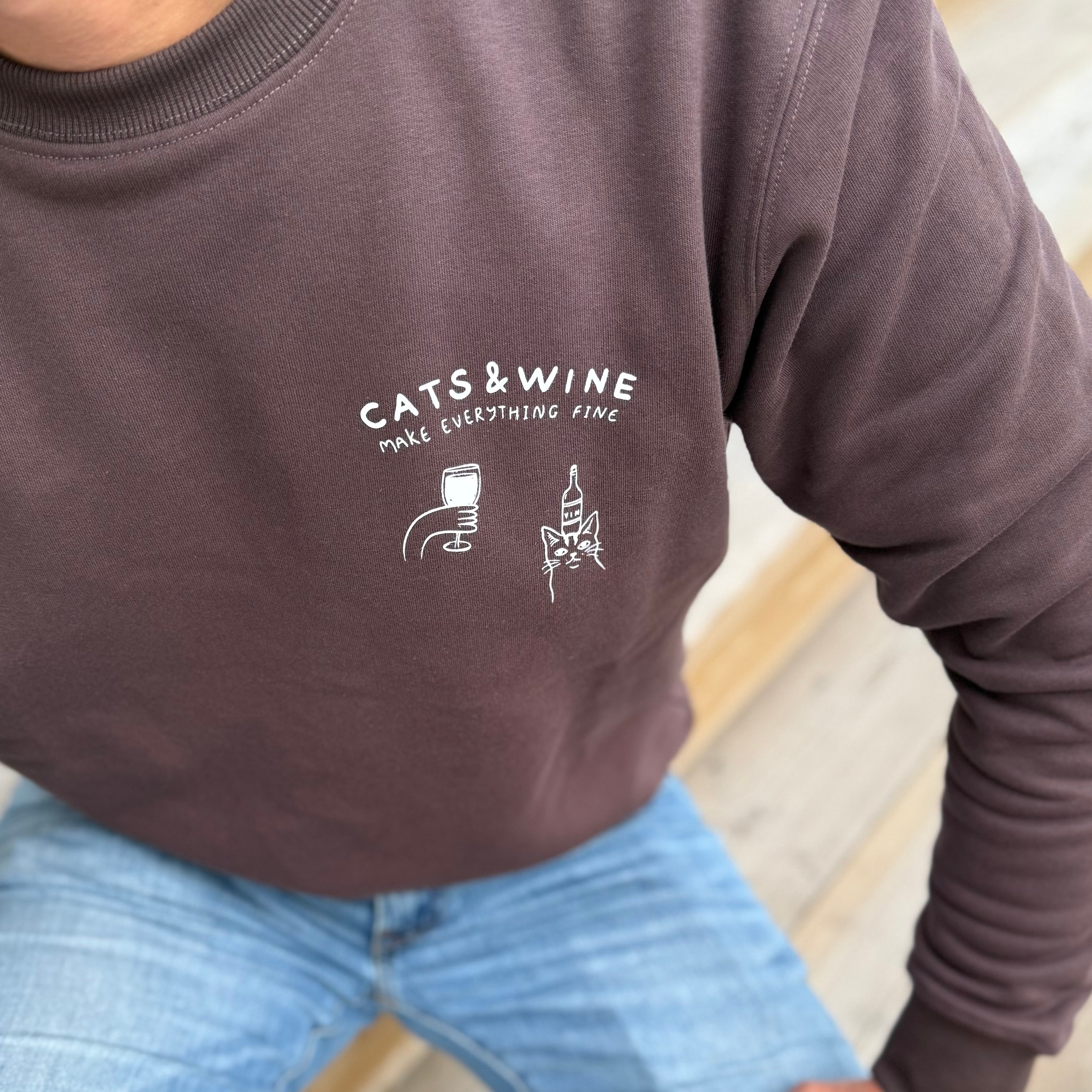 Person wearing a brown sweatshirt with 'Cats & Wine Make Everything Fine' text and graphics.