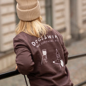 Person wearing a brown sweatshirt with 'DOGS & WINE ME EVERYTHING FINE' text and graphics.