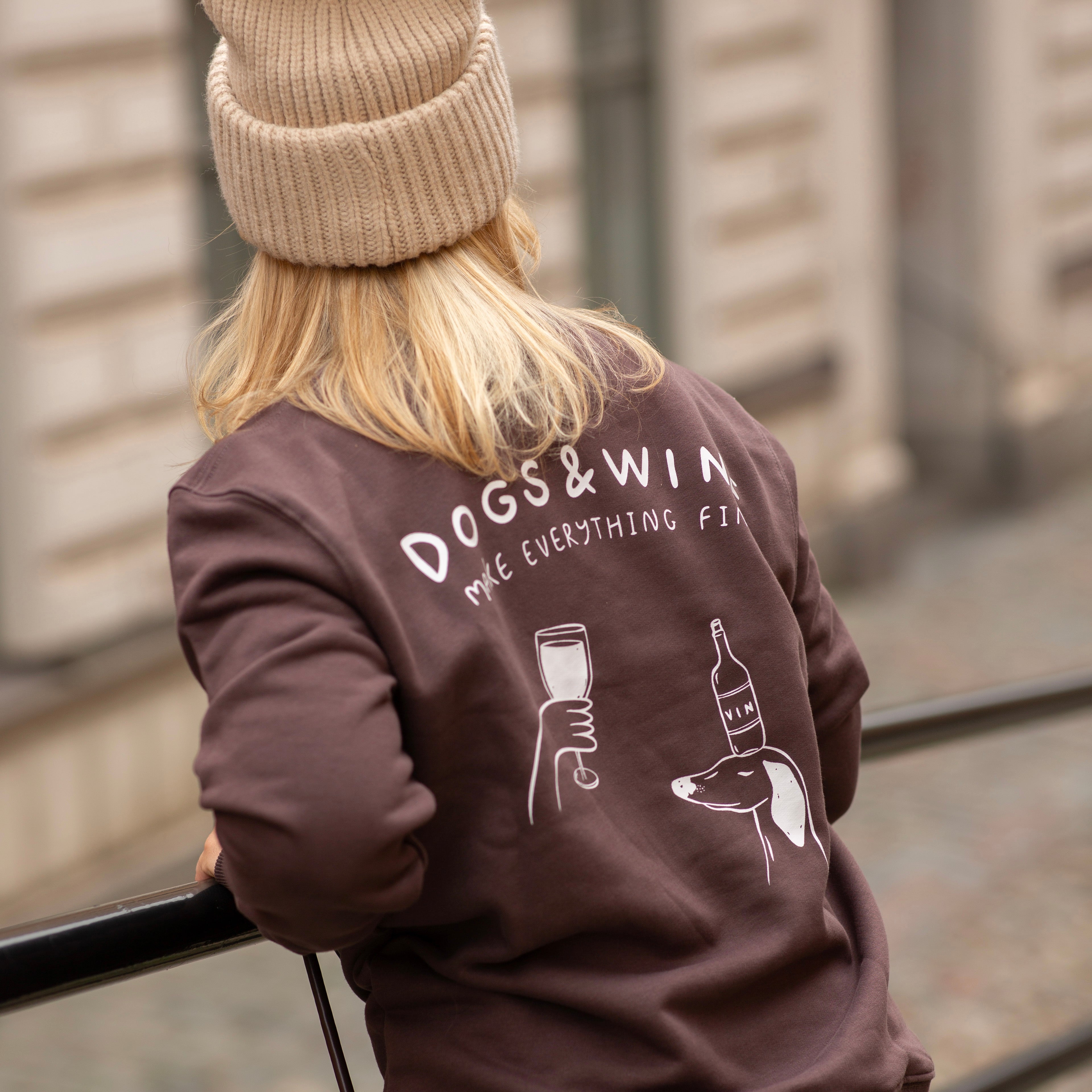 Person wearing a brown sweatshirt with 'DOGS & WINE ME EVERYTHING FINE' text and graphics.